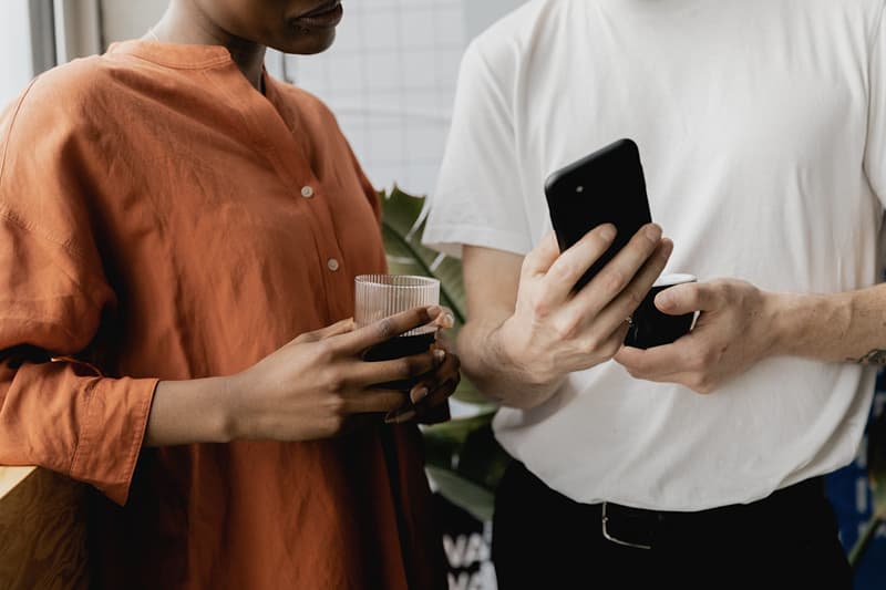 Two people in conversation, one holding a glass and another a smartphone, with only their torsos visible.