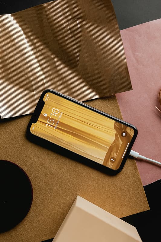 A smartphone charging on a desk displays a golden wood-textured wallpaper among aesthetically arranged papers